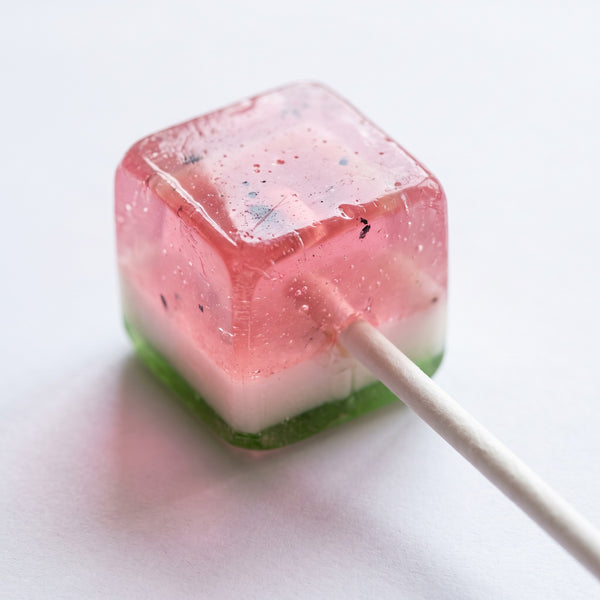 Watermelon flavored cube-shaped lollipop on a white stick